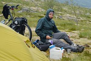 Thomas Meixner vor seinem Zelt sitzend, mit fest zugeschnürter Kapuze als Mückenschutz